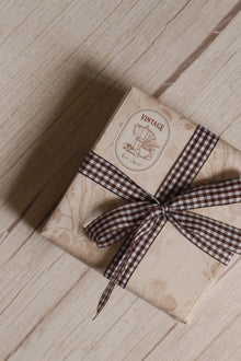 A vintage-style gift parcel tied with Cortado Checks Ribbon, showing the brown and white checked ribbon styled as a bow for warm and thoughtful packaging.
