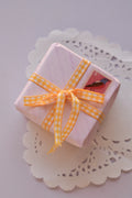 A small gift parcel tied with Mango Gingham Checkered Ribbon, showing the yellow and white checkered ribbon styled as a cheerful bow for thoughtful packaging.