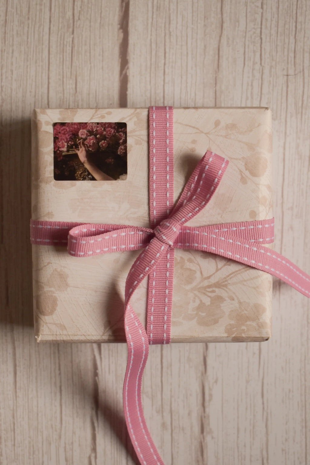 A vintage-style gift parcel tied with Rosette Stitches Ribbon, showing the pink ribbon with white stitched detail styled as a thoughtful bow.