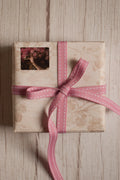 A vintage-style gift parcel tied with Rosette Stitches Ribbon, showing the pink ribbon with white stitched detail styled as a thoughtful bow.
