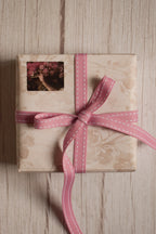 A vintage-style gift parcel tied with Rosette Stitches Ribbon, showing the pink ribbon with white stitched detail styled as a thoughtful bow.