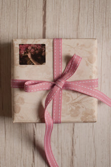 A vintage-style gift parcel tied with Rosette Stitches Ribbon, showing the pink ribbon with white stitched detail styled as a thoughtful bow.