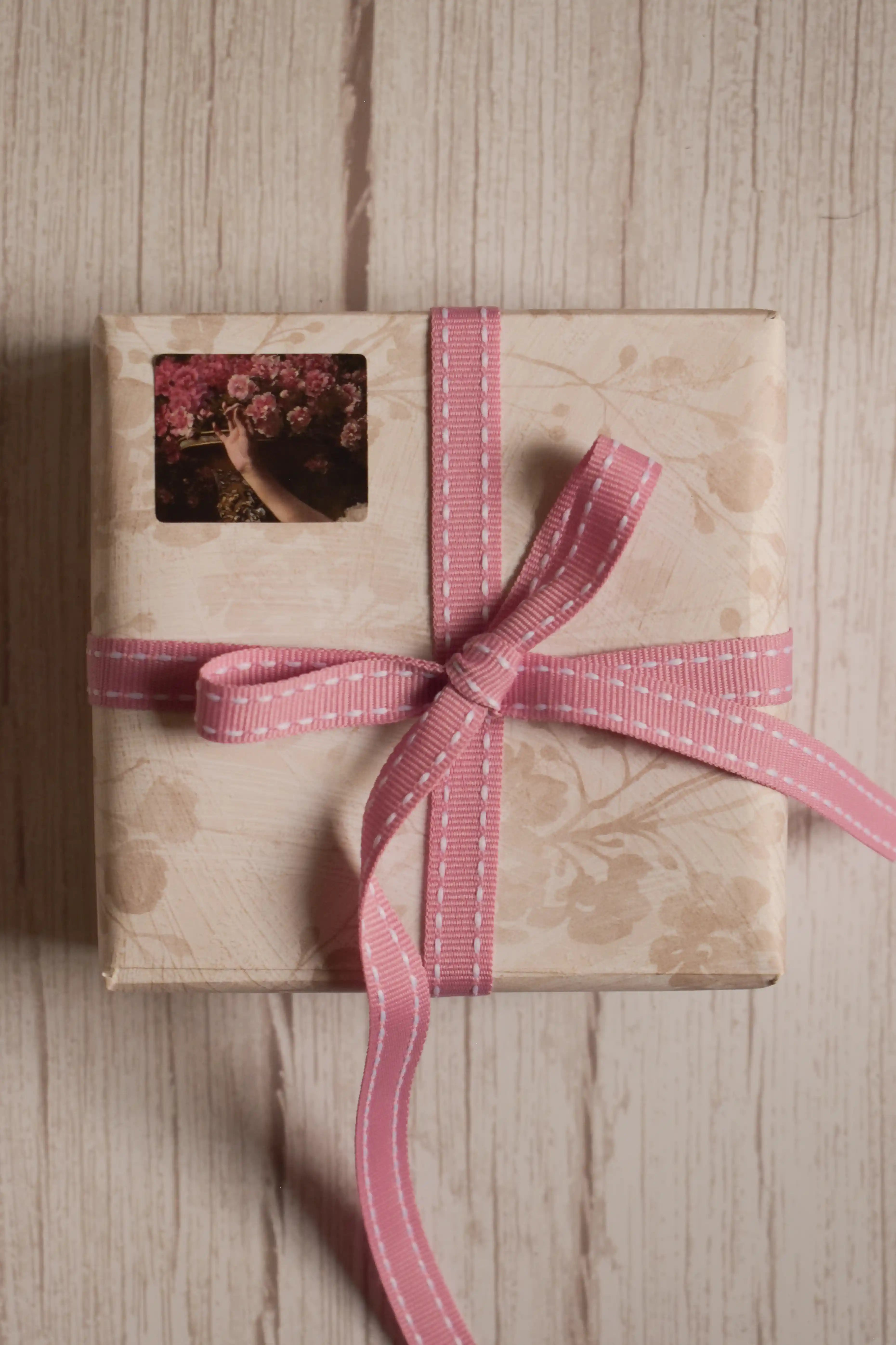 A vintage-style gift parcel tied with Rosette Stitches Ribbon, showing the pink ribbon with white stitched detail styled as a thoughtful bow.
