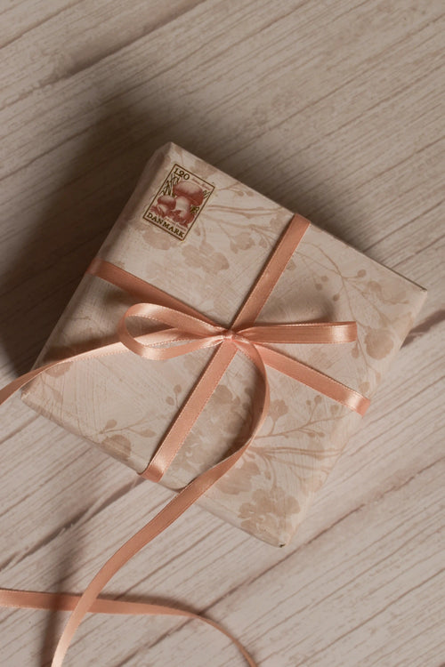 A vintage-style gift parcel wrapped in soft floral paper and tied with an Apricot Satin Ribbon bow, showing how the ribbon can be used for elegant gift packaging.