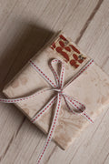 A vintage-style gift parcel tied with Candy Seam Narrow Ribbon, showing the white ribbon with red stitched detail styled as a small bow for gift packaging.