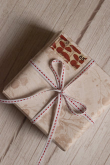 A vintage-style gift parcel tied with Candy Seam Narrow Ribbon, showing the white ribbon with red stitched detail styled as a small bow for gift packaging.