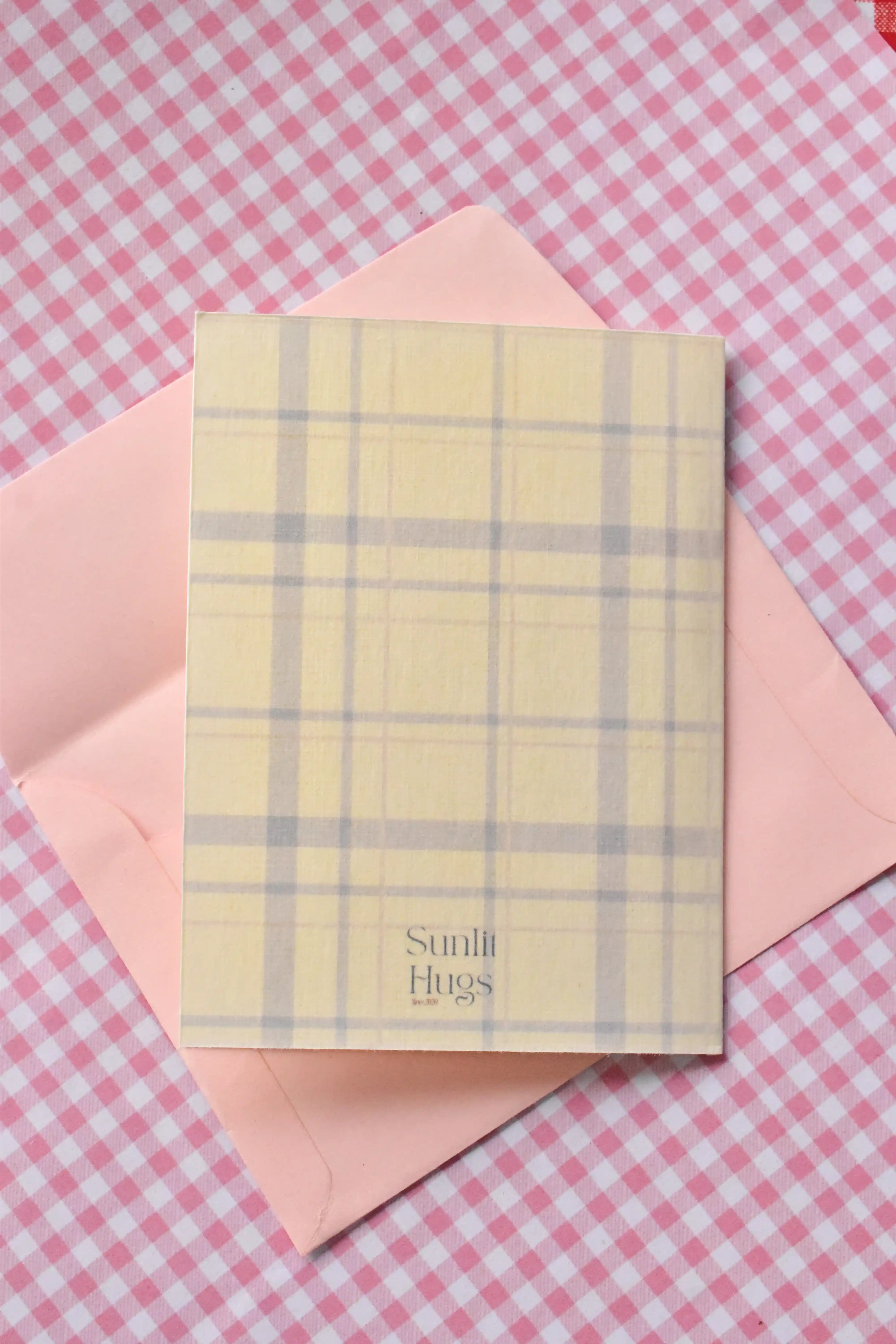 This image displays the back of the 'Glowing Girl Era' card, showing the continuous light purple and white plaid pattern and the Sunlit Hugs brand logo.