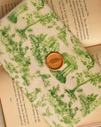 A detailed view highlighting the rich golden wax seal and its delicate leaf design, showcasing the meticulous craftsmanship over the green toile architectural print.