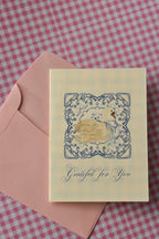 This image shows the front of the Grateful For You card, capturing its delicate blue lace and swan design. The serene look sets a warm tone, ready for your note of appreciation, with the pink envelope nearby.