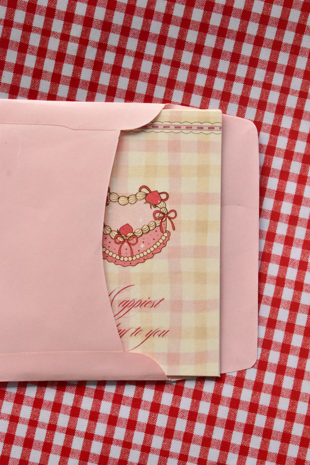 This view captures the Happiest Birthday to You card being gently placed into the pink envelope. It demonstrates the presentation, with the sweet pink heart-shaped cake illustration peeking out as it awaits its recipient.