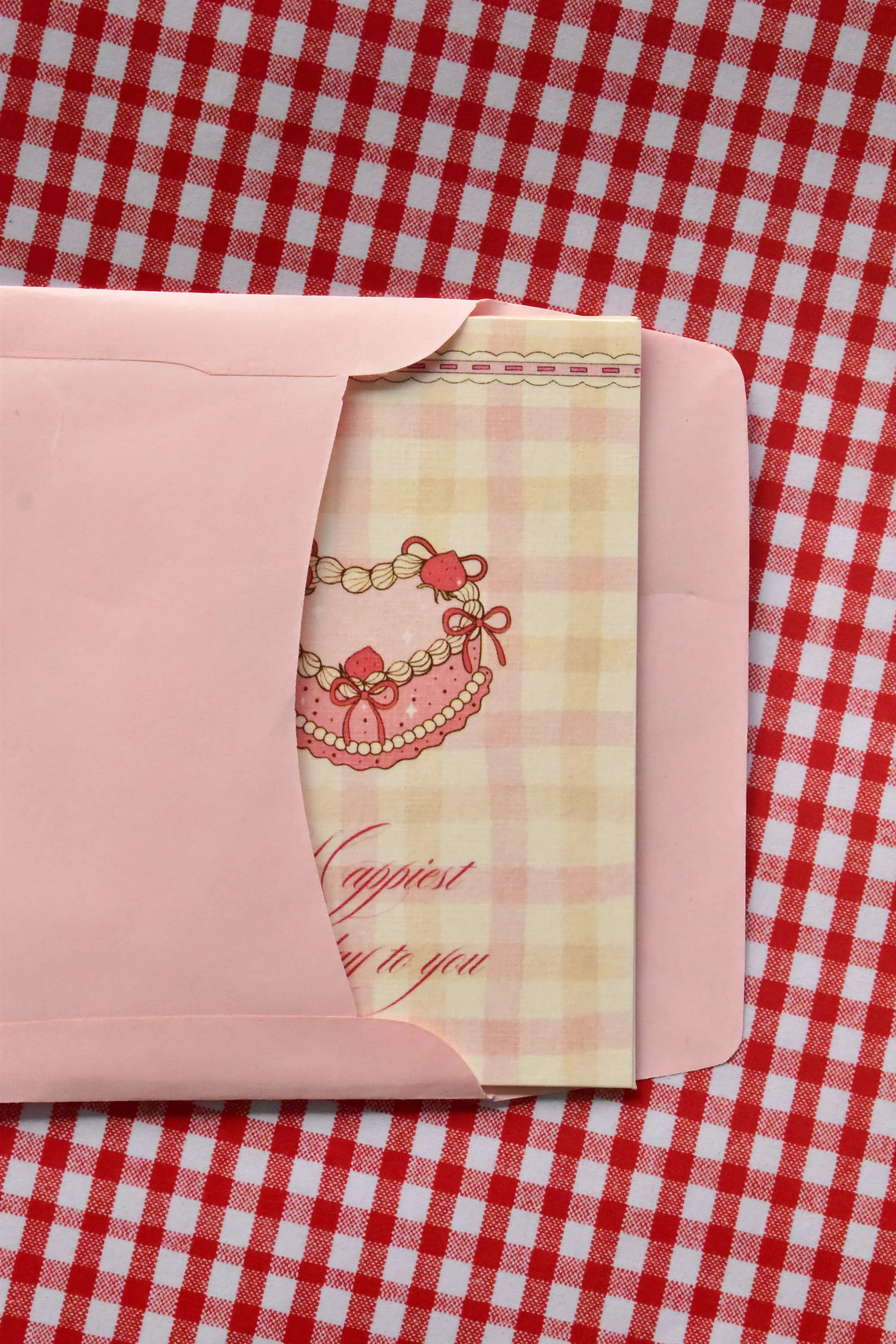 This view captures the Happiest Birthday to You card being gently placed into the pink envelope. It demonstrates the presentation, with the sweet pink heart-shaped cake illustration peeking out as it awaits its recipient.