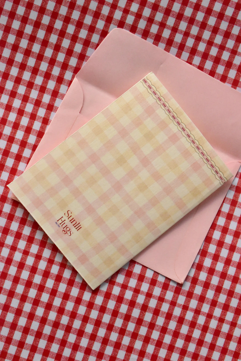 This image displays the back of the 'Happiest Birthday To You' card, highlighting the soft pink and cream gingham design and the Sunlit Hugs logo.