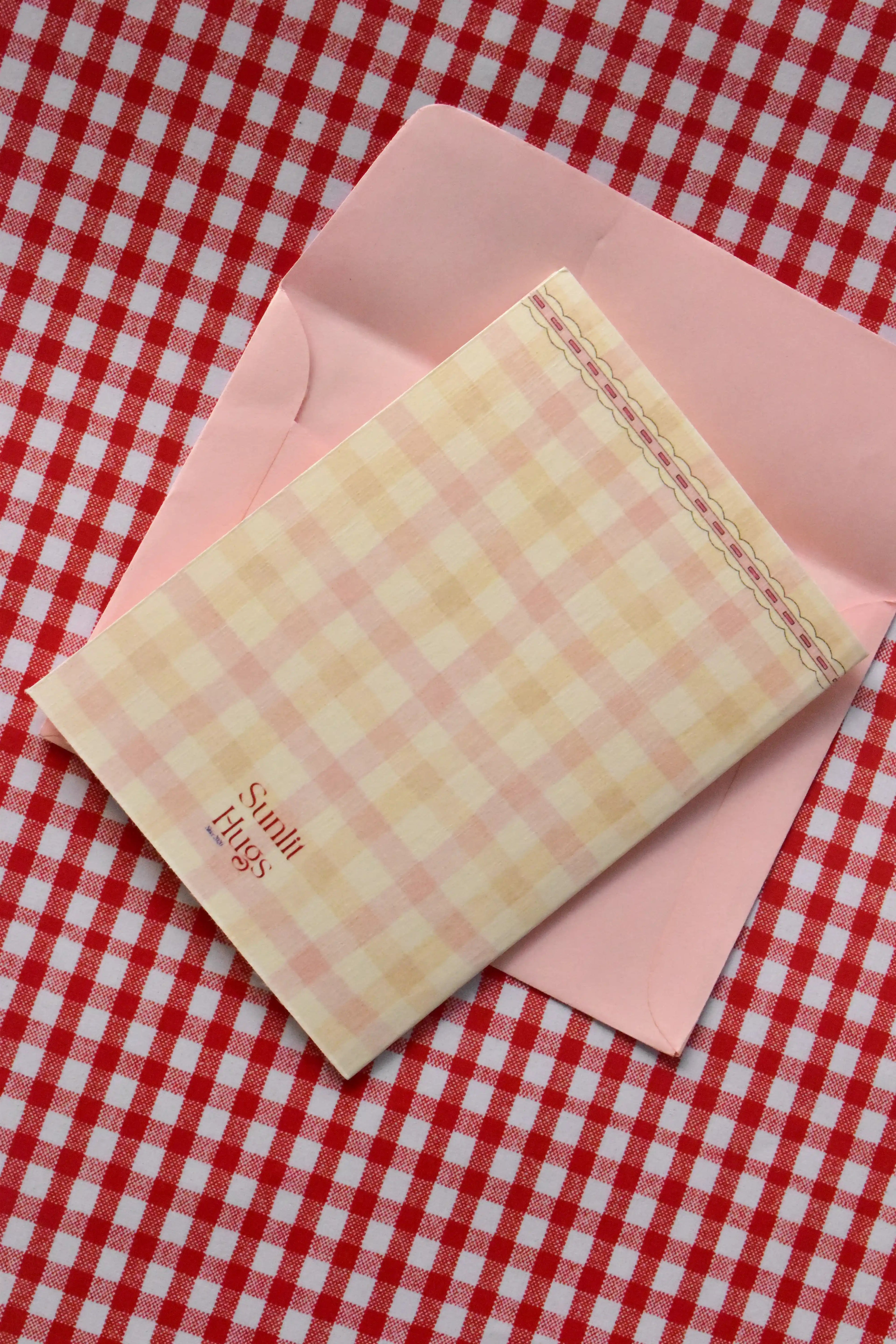 This image displays the back of the 'Happiest Birthday To You' card, highlighting the soft pink and cream gingham design and the Sunlit Hugs logo.