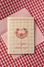This image showcases the Happiest Birthday To You card, highlighting the sweet pink heart-shaped cake design and the cosy pink gingham pattern for pure birthday joy.