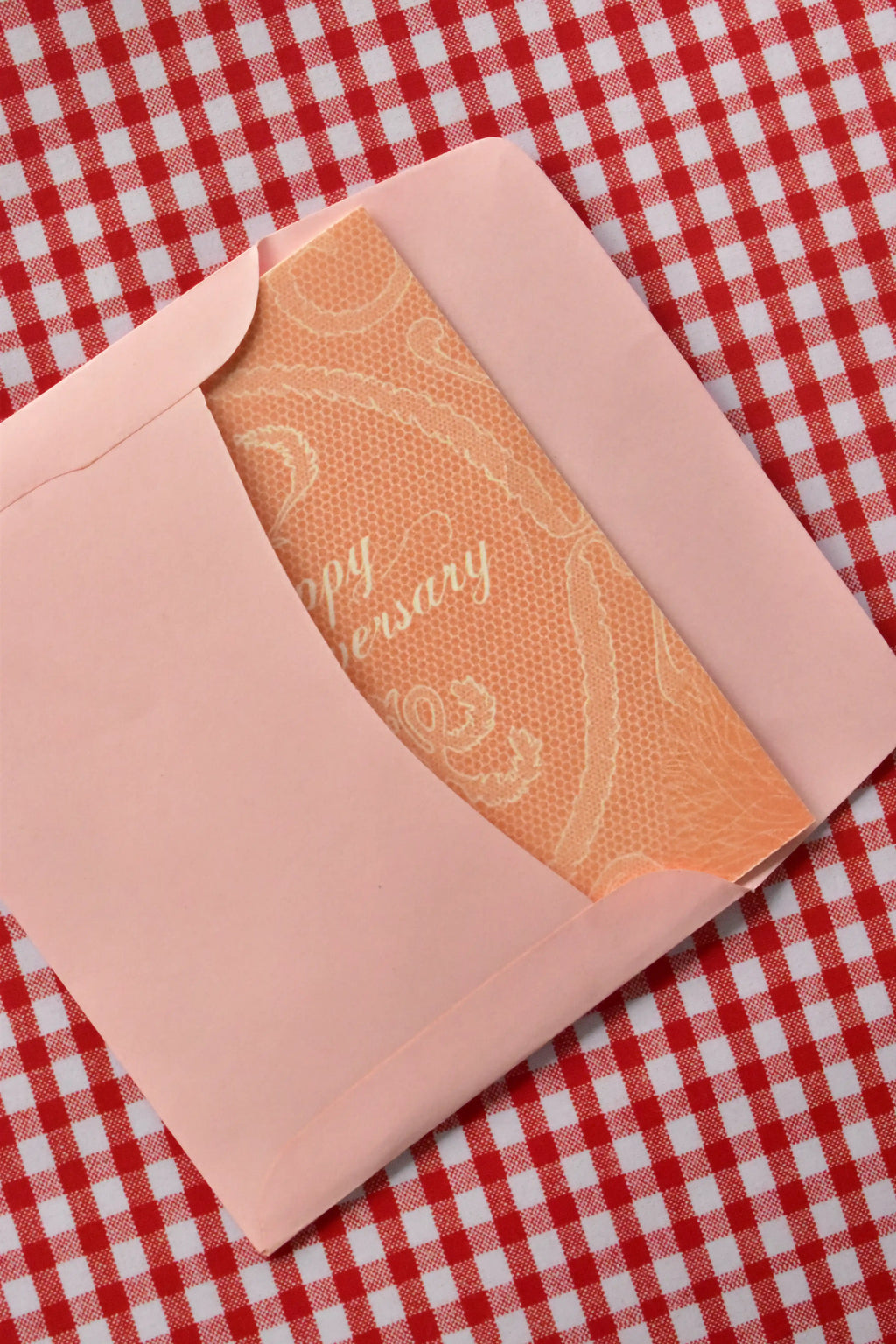 This view captures the Happy Anniversary card being neatly placed into the pink envelope. It demonstrates the presentation, with the elegant peach lace design peeking out as it is prepared for sending a heartfelt message.