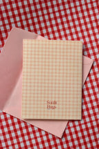 A clear view of the back of the 'Happy Birthday Cutie' card, displaying the continuous pink and cream gingham design and the Sunlit Hugs brand logo.