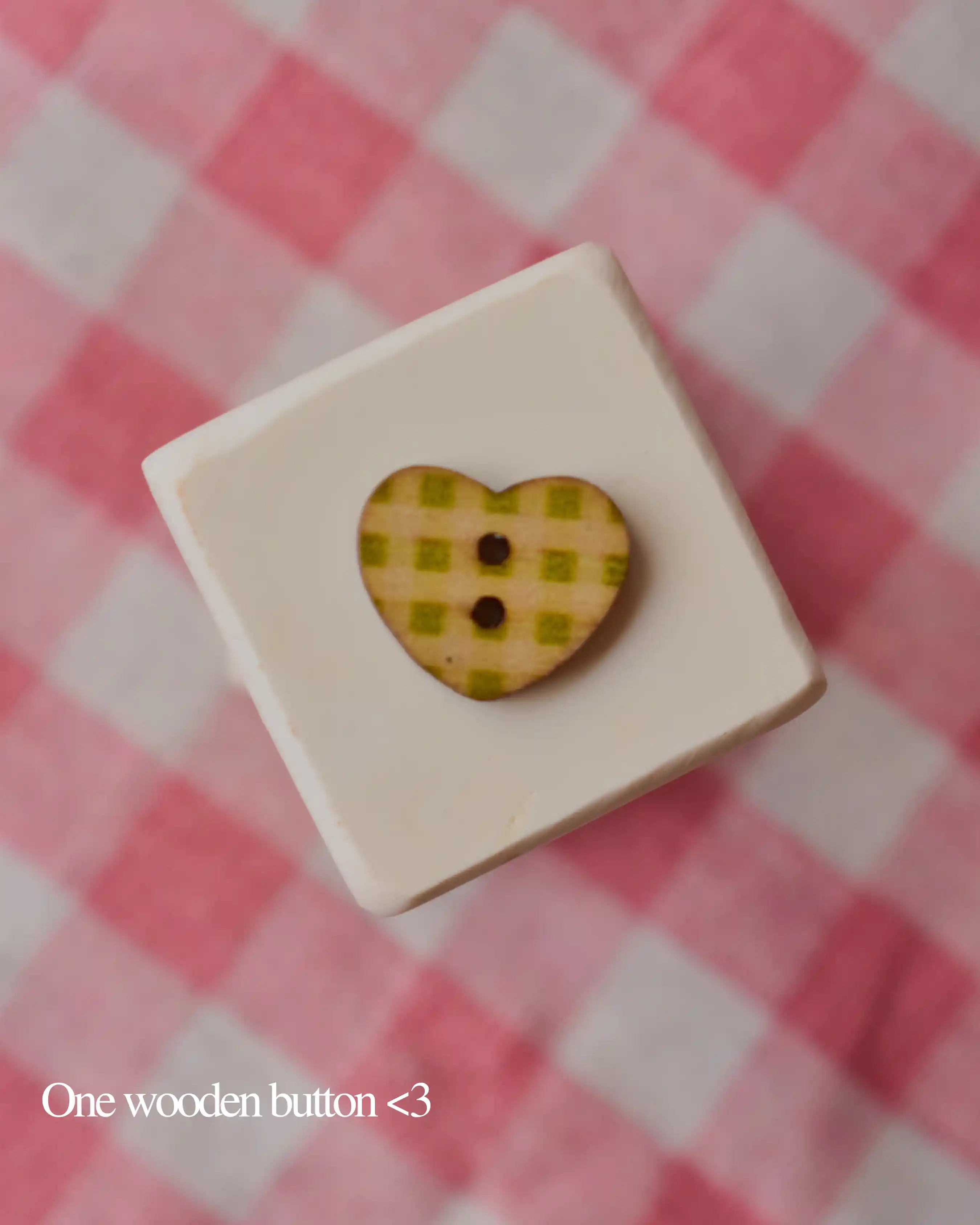 One heart-shaped wooden button with a green and yellow plaid pattern, resting on a white block.