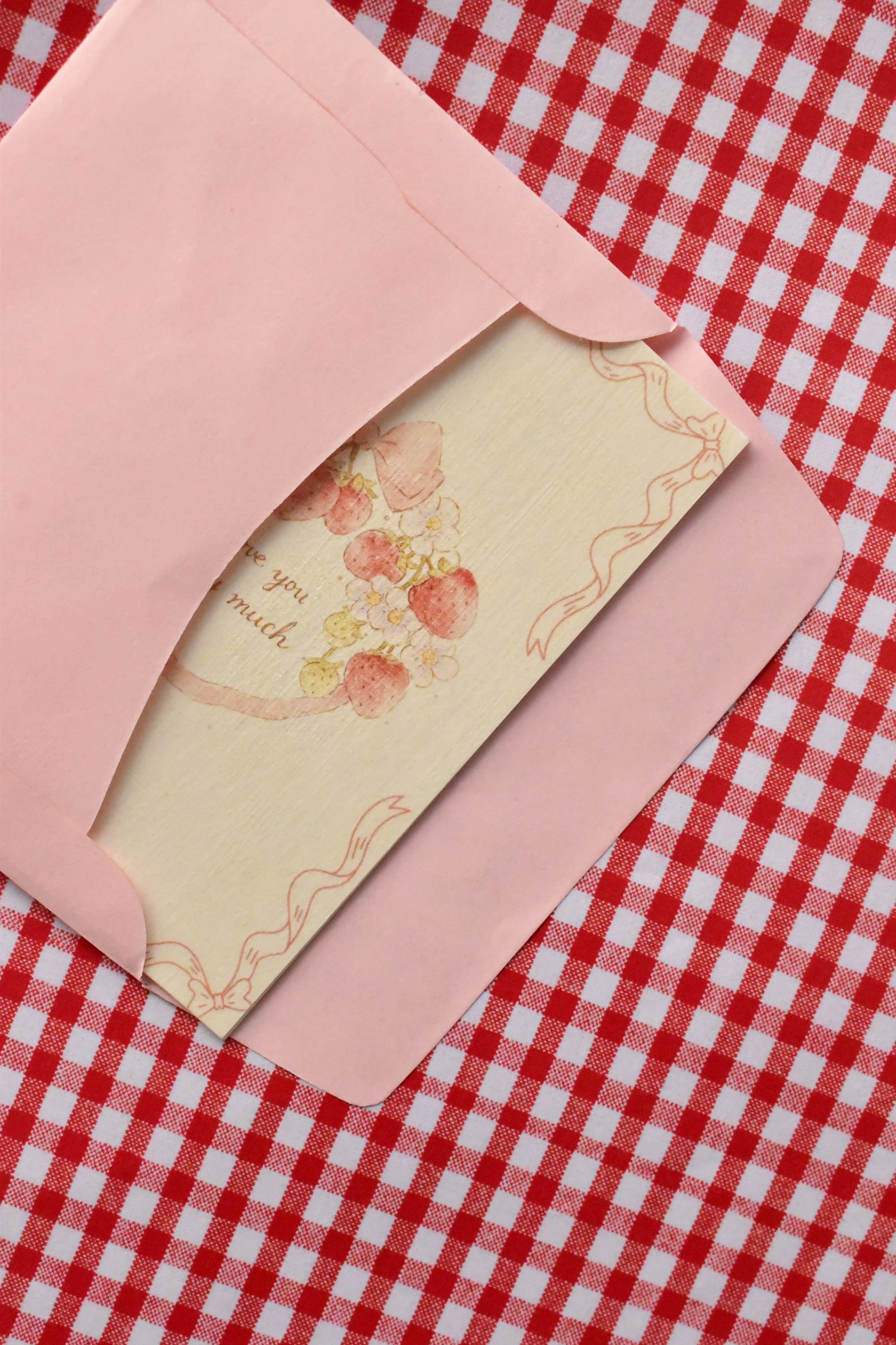This view captures the Love You Berry Much card being gently placed into the pink envelope. It demonstrates the presentation, with the sweet strawberry wreath illustration peeking out as it awaits its recipient with a loving message.
