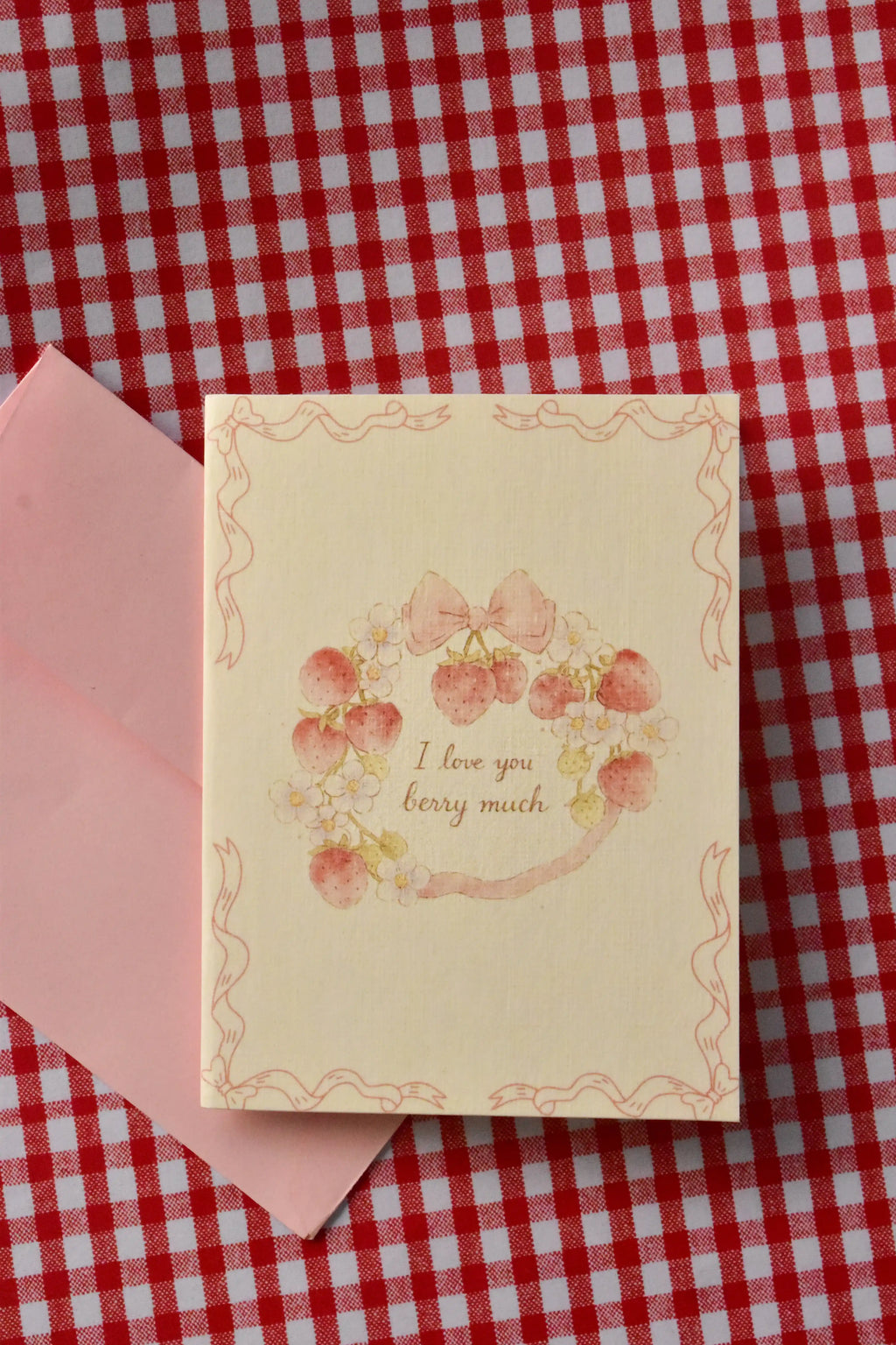 This detailed shot focuses on the sweet, intricate strawberry wreath, bow, and flower design. The cream background beautifully offsets the soft pink and red tones of the illustration, creating a warm, nostalgic feel.