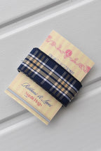 This detailed, head-on view of the Midnight Plaid ribbon highlights its refined navy and white plaid pattern. The ribbon is wrapped tidily around the "Sunlit Hugs" brand tag to show its precise design and colours.