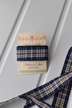 This image shows a beautifully wrapped gift box, featuring the Midnight Plaid ribbon tied into an elegant bow. The ribbon's sophisticated navy and white plaid pattern adds a classic touch to the present.