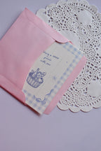 The Mini Wishing Picnics Card being gently tucked into the pink envelope, showing the blue gingham and basket illustration.