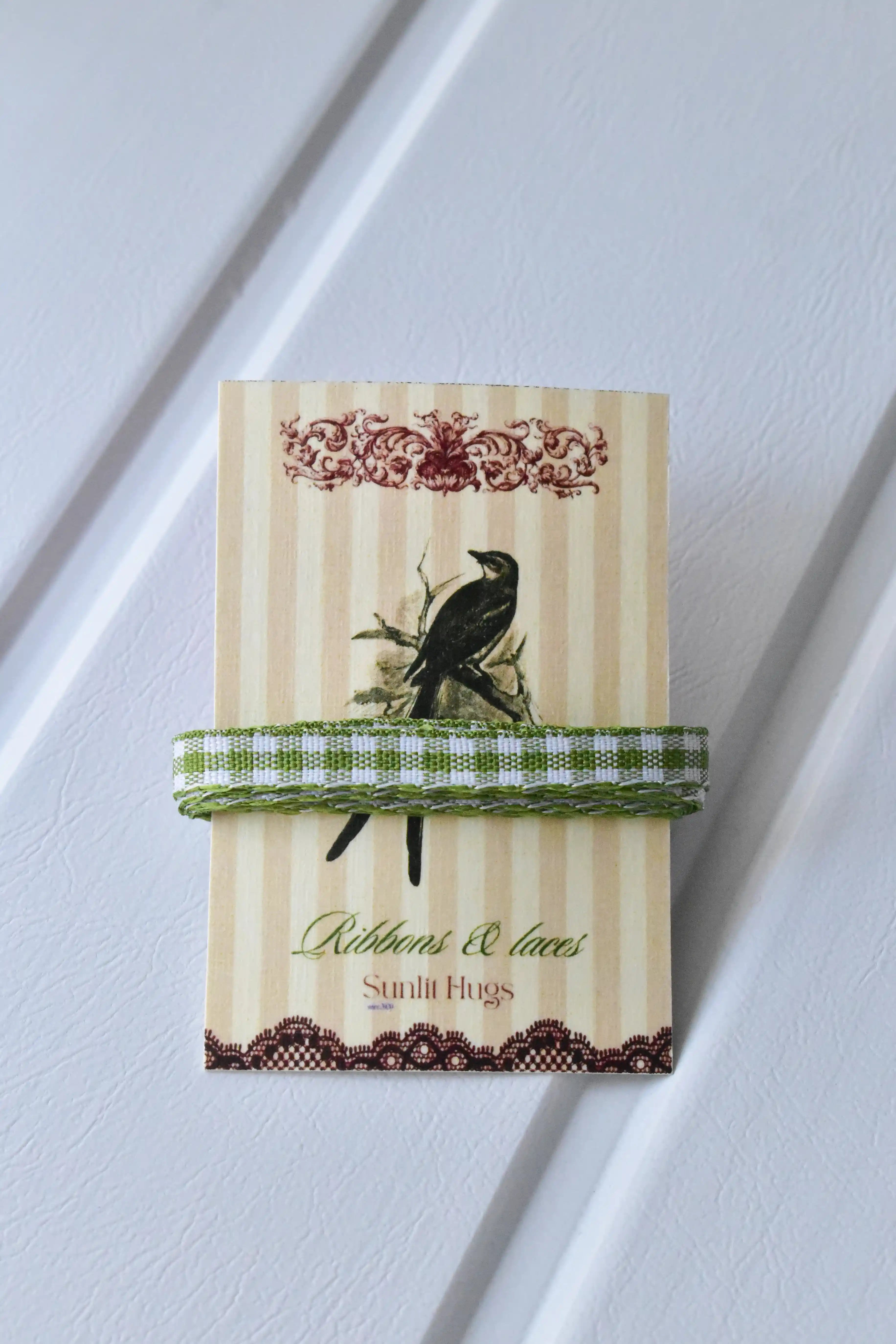 This detailed, head-on view of the Pine Picnic ribbon highlights its charming green and white checkered pattern. The ribbon is wrapped tidily around the "Sunlit Hugs" brand tag to show its precise design and colours.