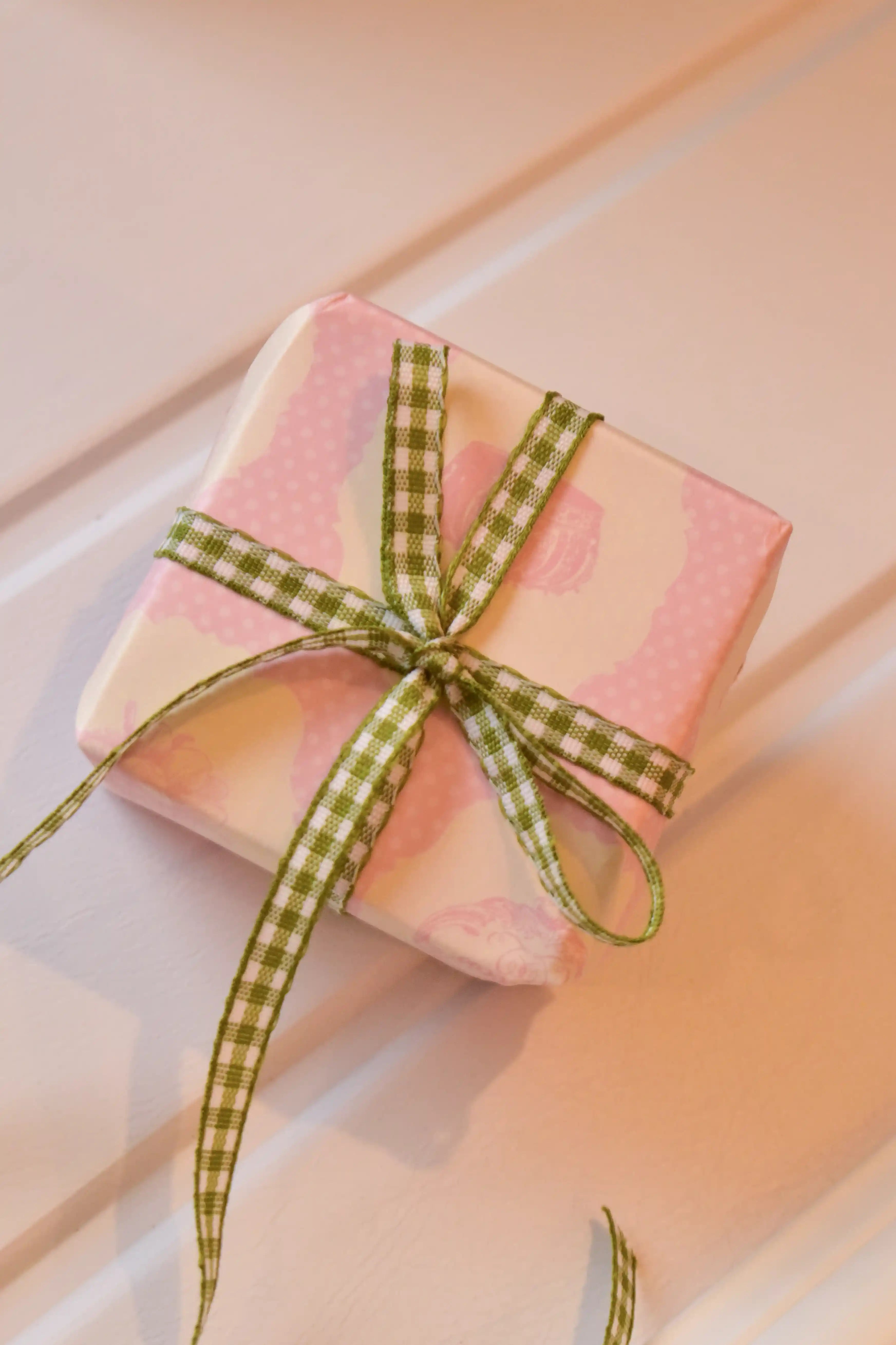 This image shows a beautifully wrapped gift box, featuring the Pine Picnic ribbon tied into a sweet bow. The ribbon's elegant green and white pattern adds a fresh and charming touch to the present.