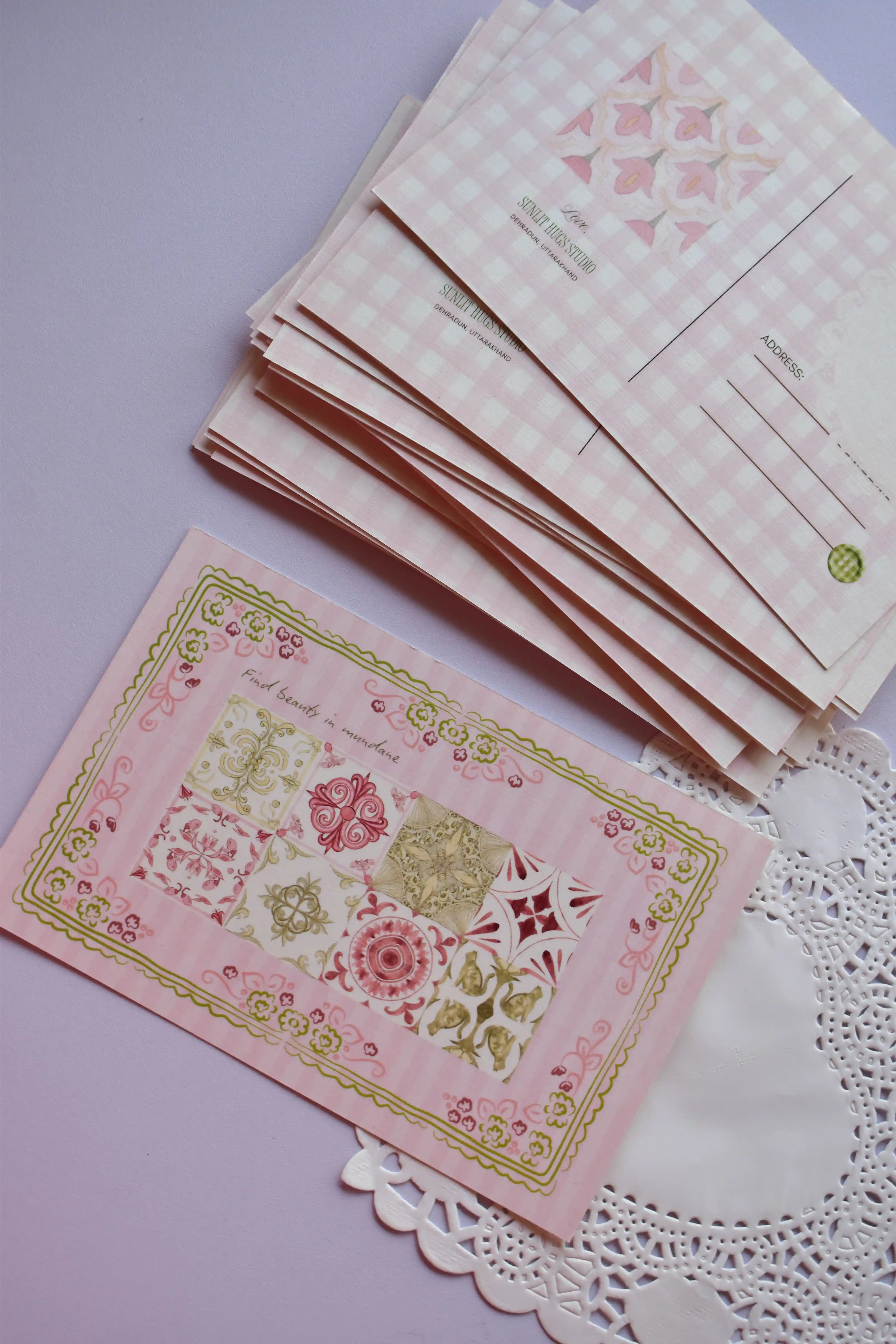 A stack of postcards showing the pink gingham reverse design on the top cards, with one card laid flat displaying the 'Find beauty in mundane' vintage pattern front. The cards have a wide pink and white check pattern.