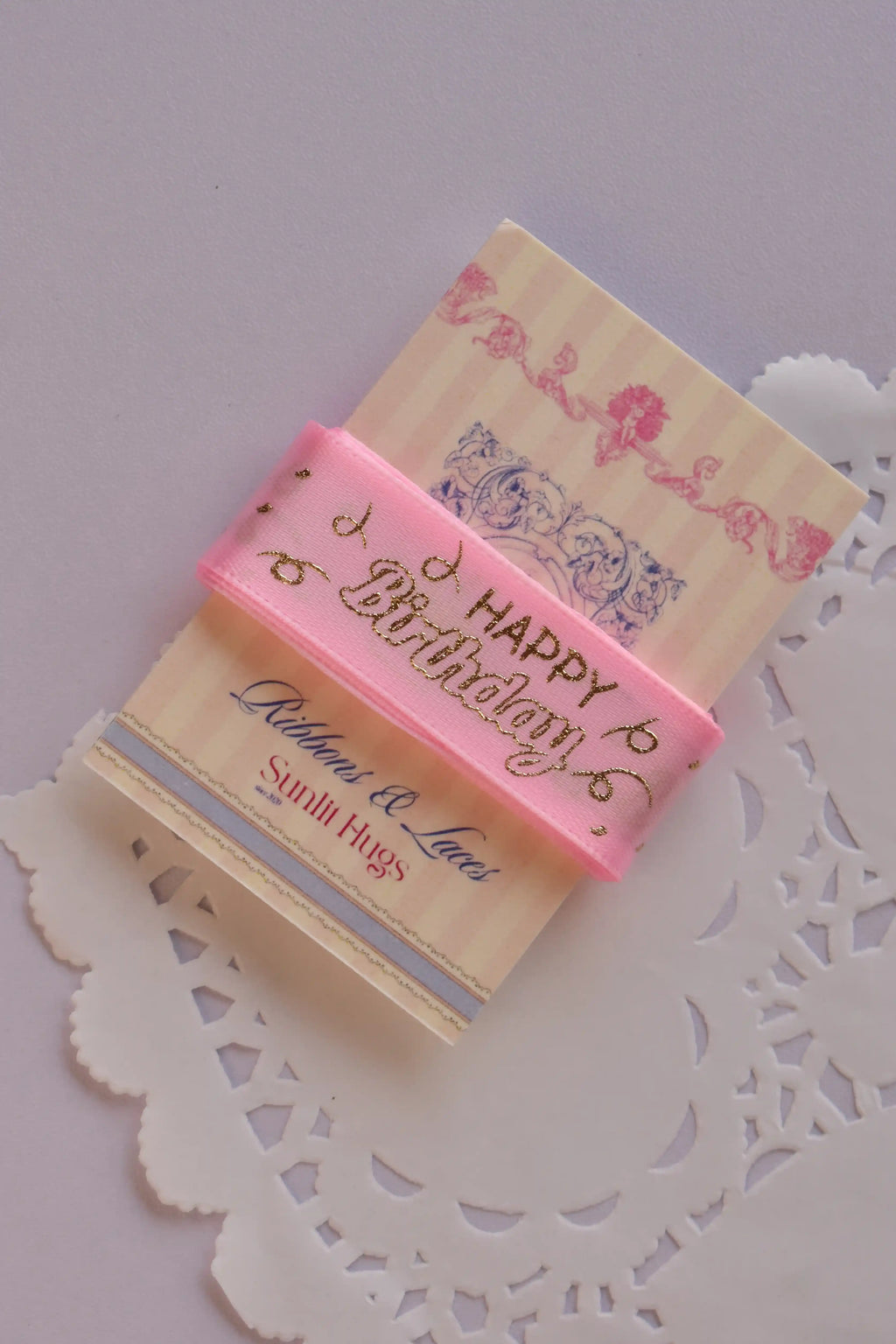 Angled view of the soft pink birthday ribbon wrapped around a "Sunlit Hugs" card, emphasizing the ribbon's texture and gold foil script.