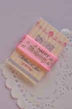 Angled view of the soft pink birthday ribbon wrapped around a "Sunlit Hugs" card, emphasizing the ribbon's texture and gold foil script.