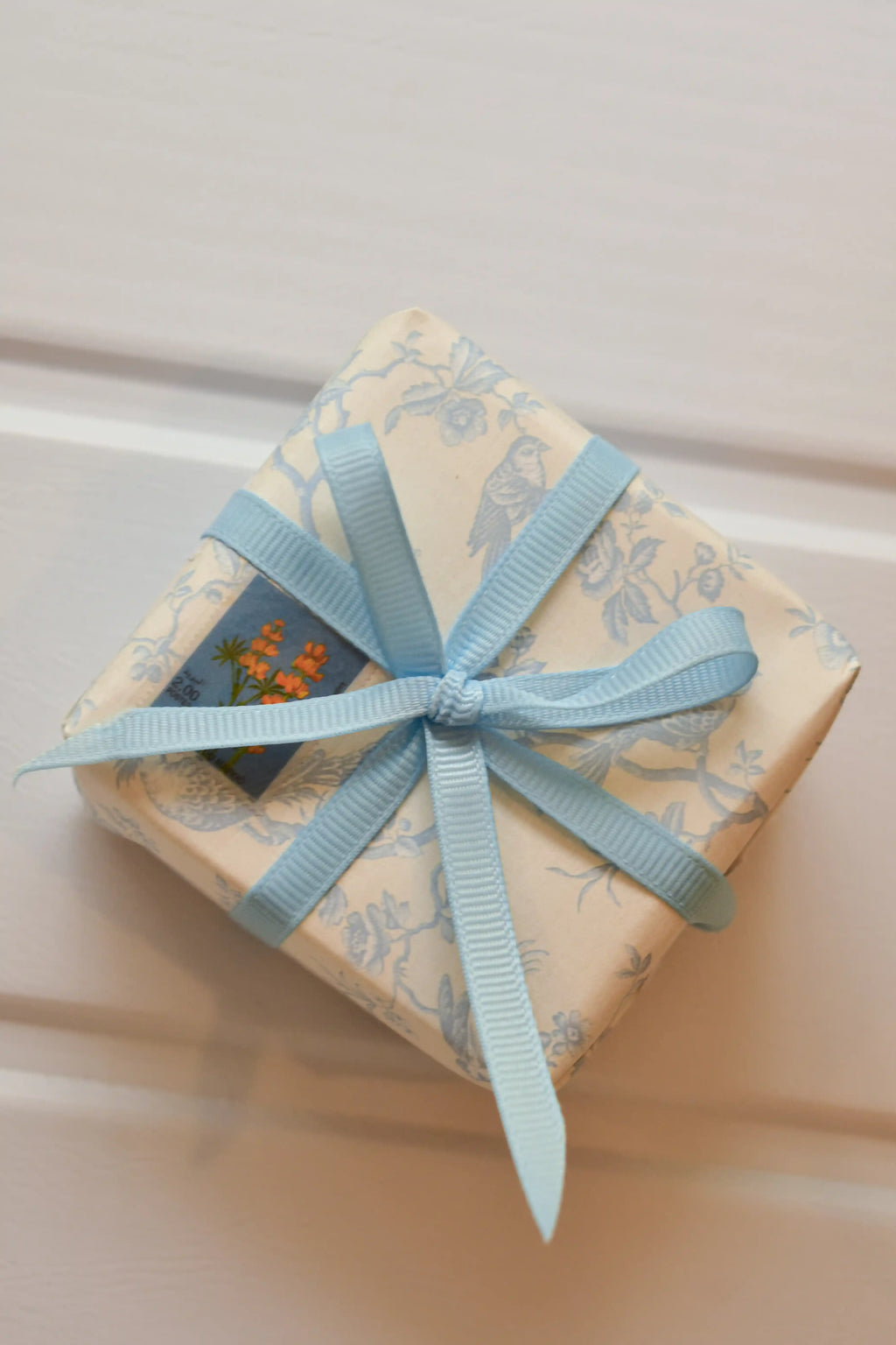 This image shows a beautifully wrapped gift box, featuring the Powder Blue Charm ribbon tied into a delicate bow. The ribbon's elegant light blue colour adds a cheerful and charming touch to the present.