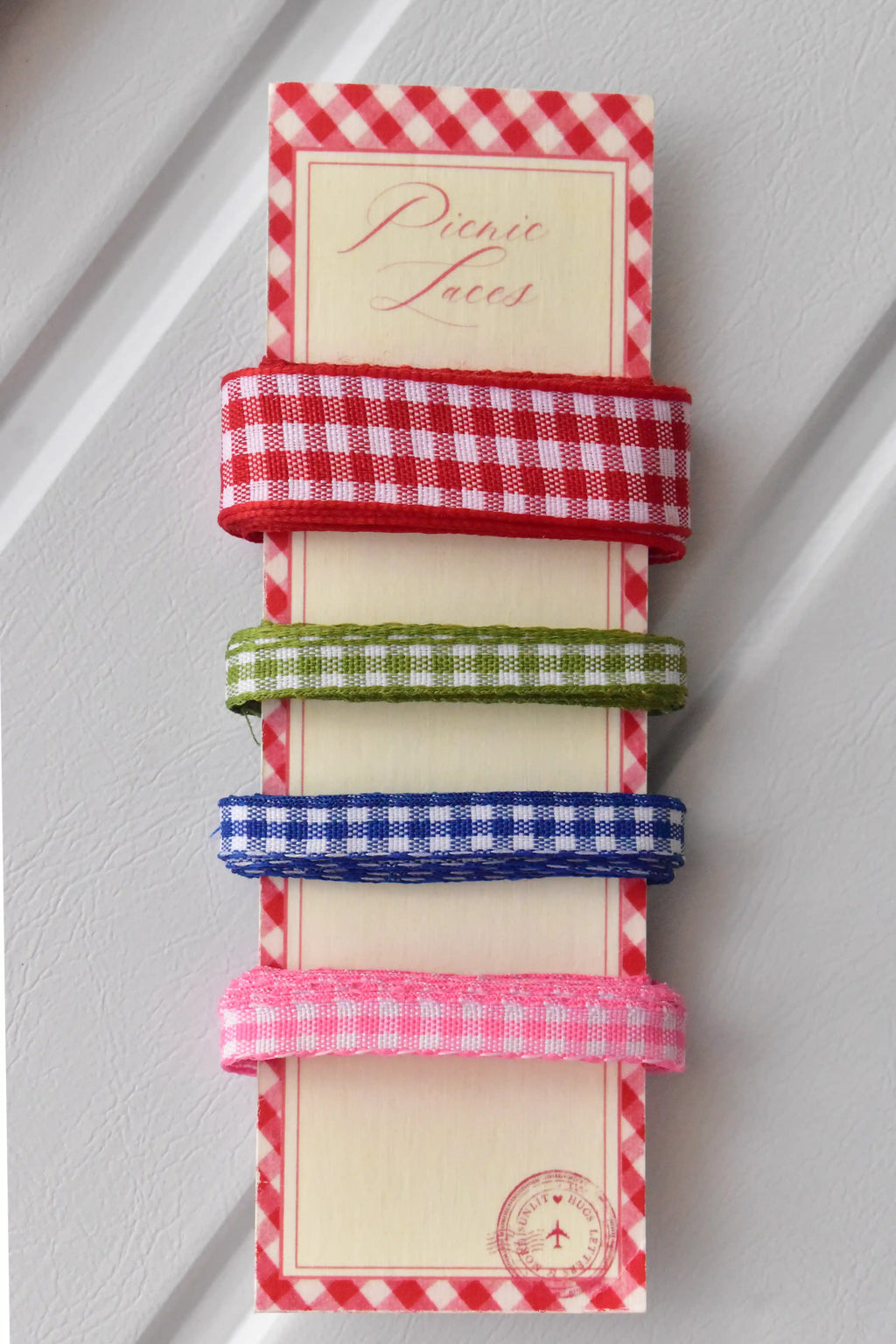 Four narrow gingham ribbons in red, green, blue, and pink, displayed vertically on a themed ribbon card.