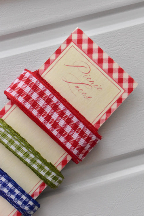 Angled close-up of the red and green narrow gingham ribbons wrapped around the top corner of the "Picnic Laces" display card.
