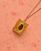 Golden vintage-style locket resting on floral pink backdrop.