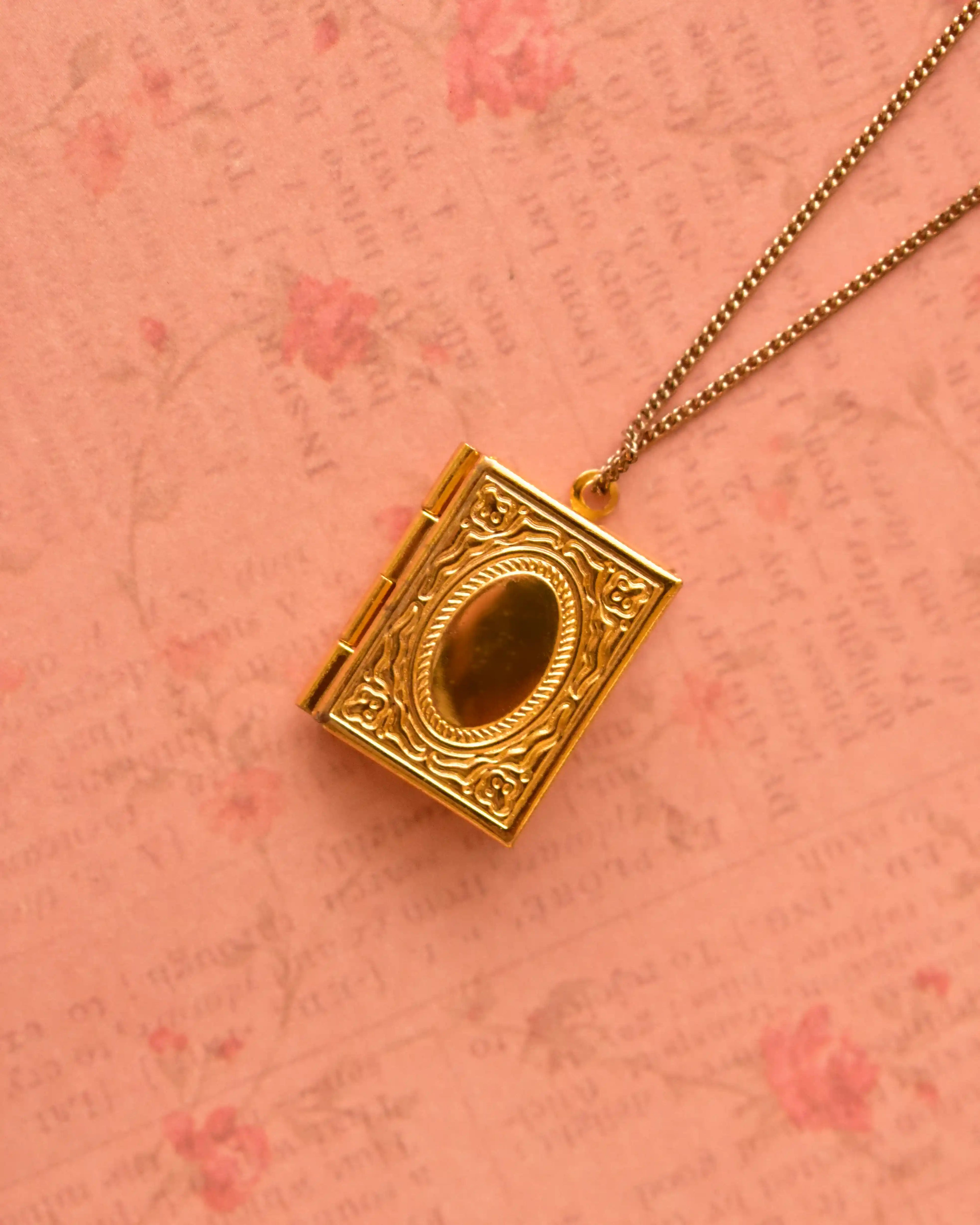 Golden vintage-style locket resting on floral pink backdrop.
