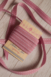 Rosette Stitches Ribbon shown with loose ribbon strands around the product card, highlighting its soft pink tone and white stitched detail for crafts and packaging.