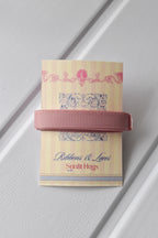 This detailed, head-on view of the Rustic Blush ribbon highlights its sophisticated rose gold colour and subtle texture. The ribbon is wrapped tidily around the "Sunlit Hugs" brand tag to show its precise design.