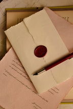 This warm, staged shot highlights the final, dramatic presentation: the scarlet wax seal securing the handmade ivory envelope, symbolizing a timeless and private act of old-world letter writing.