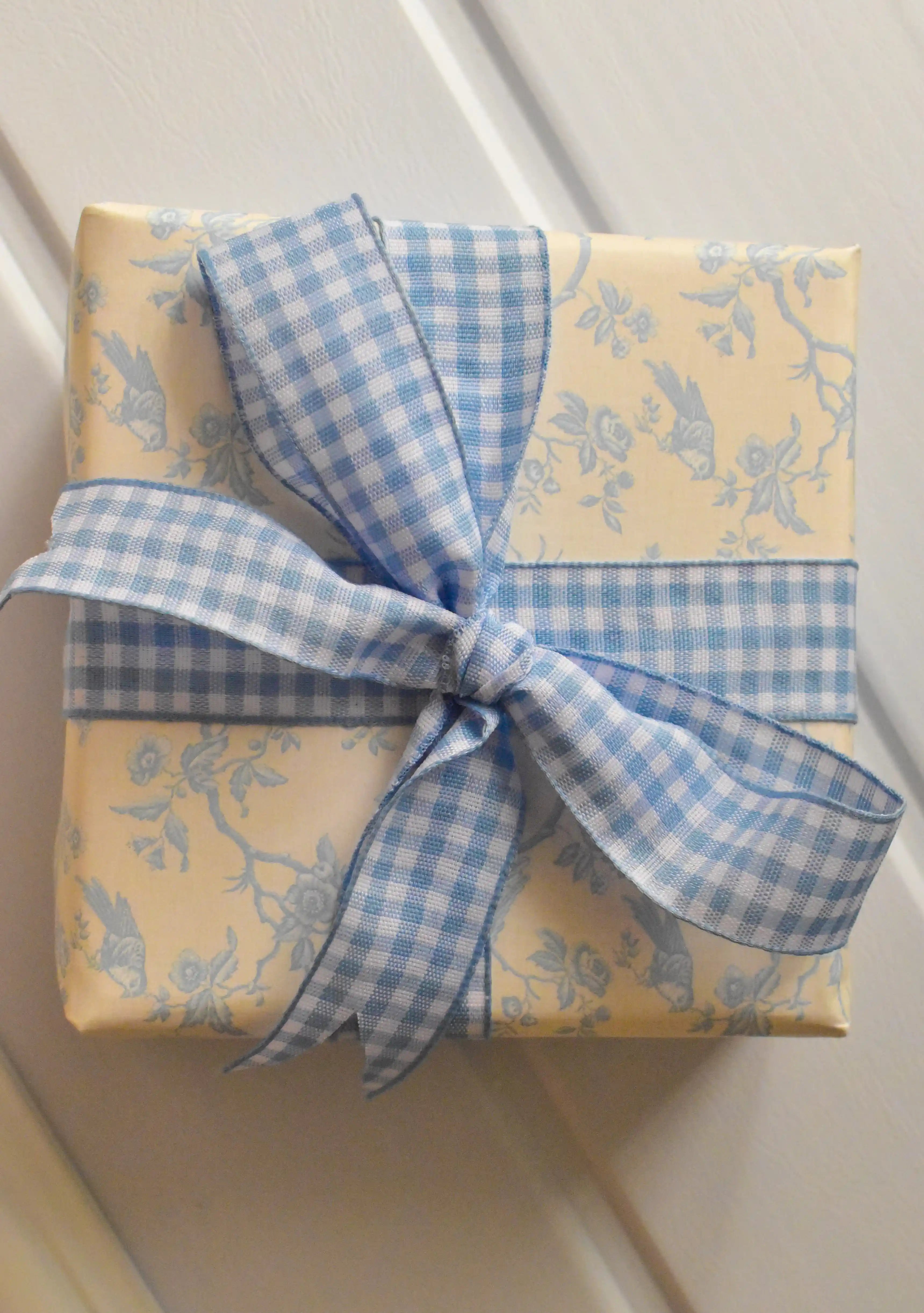This image shows a beautifully wrapped gift box, featuring the Sky Gingham ribbon tied into a large, elegant bow. The ribbon's classic blue and white pattern adds a serene and charming touch to the present.