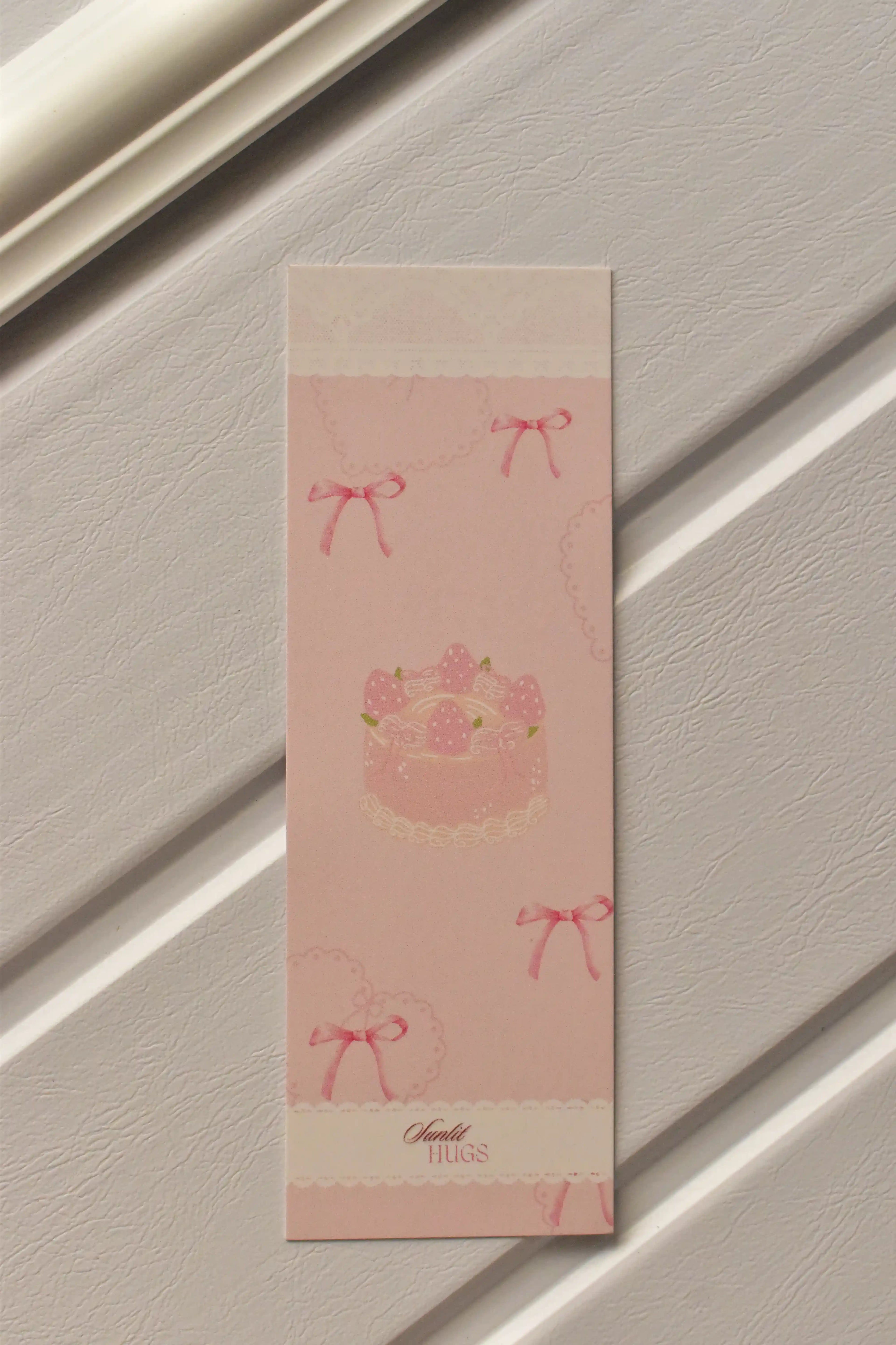 This image shows a close-up of the Cake Bookmark front, highlighting the charming pastel pink colour and sweet strawberry cake design with a delicate lace border.