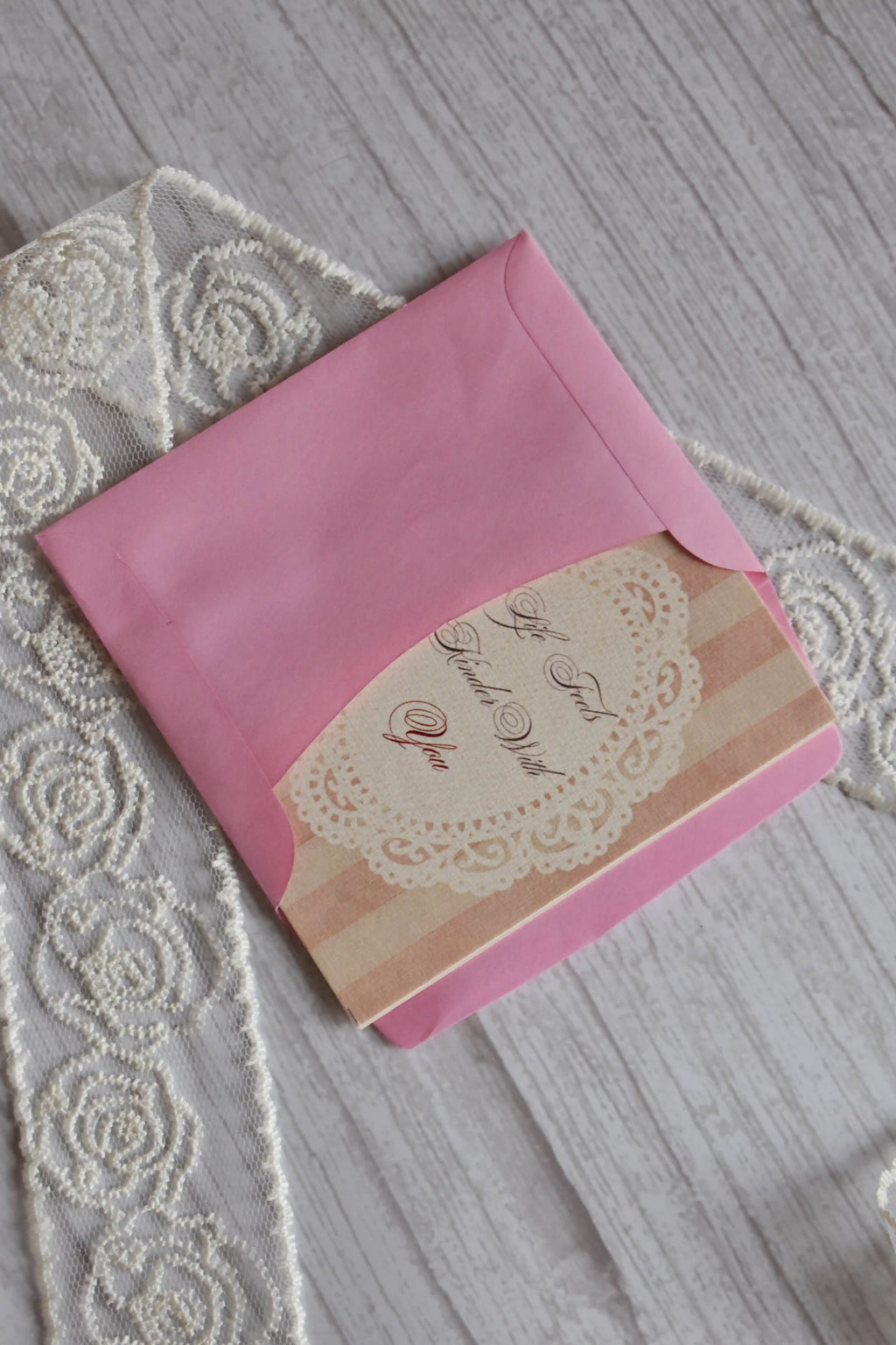 Sunlit Hugs Life Feels Kinder With You Greeting Card partially tucked inside a bright pink envelope, highlighting the elegant calligraphy and vintage lace graphic.
