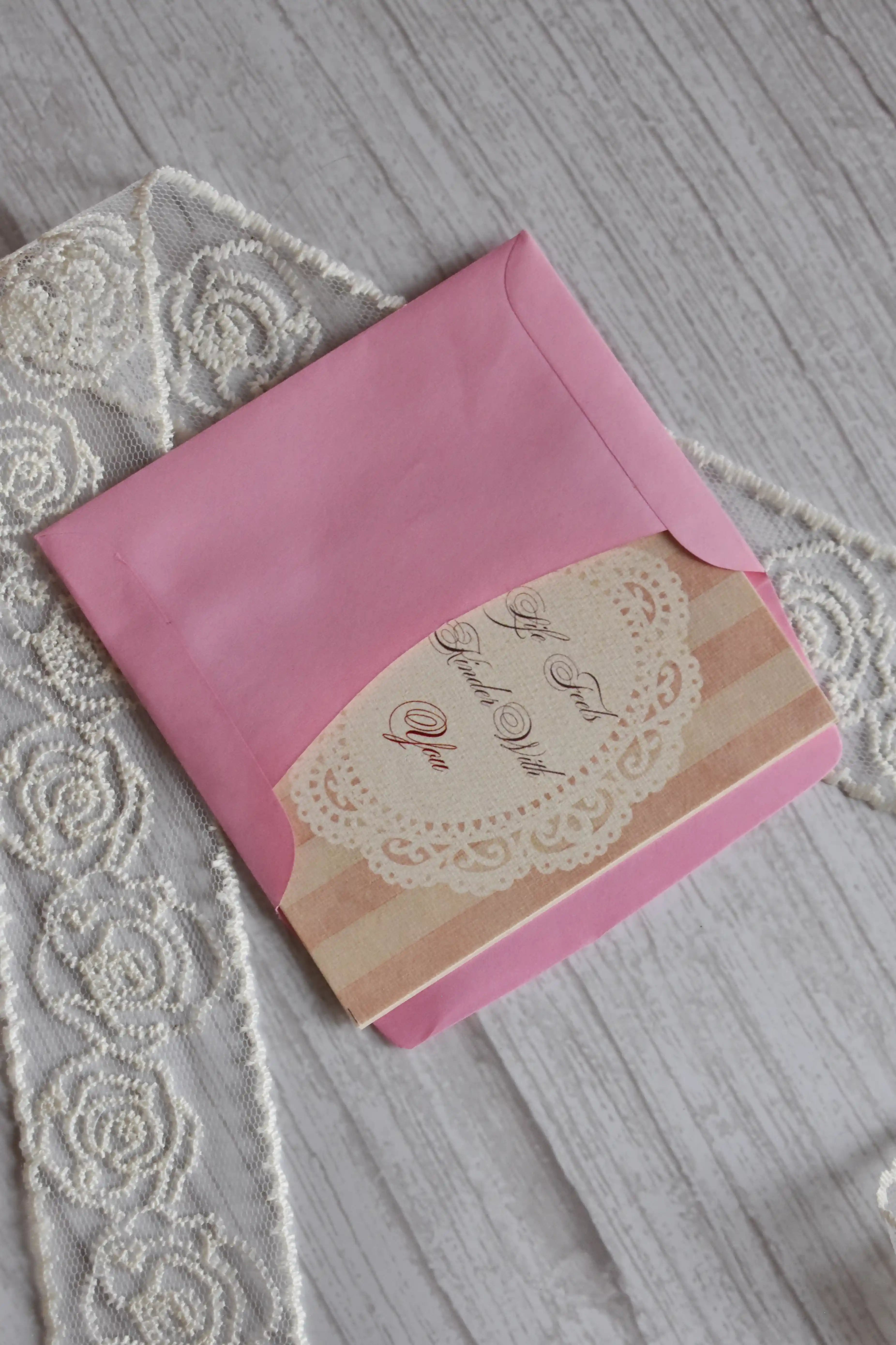 Sunlit Hugs Life Feels Kinder With You Greeting Card partially tucked inside a bright pink envelope, highlighting the elegant calligraphy and vintage lace graphic.