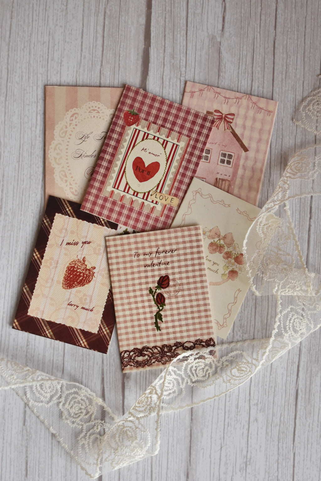 Angled view of the Sunlit Hugs Set of 6 Love Series Cards bundle showcasing various romantic greetings including "To my forever valentine" and "I miss you berry much" alongside delicate white floral lace.