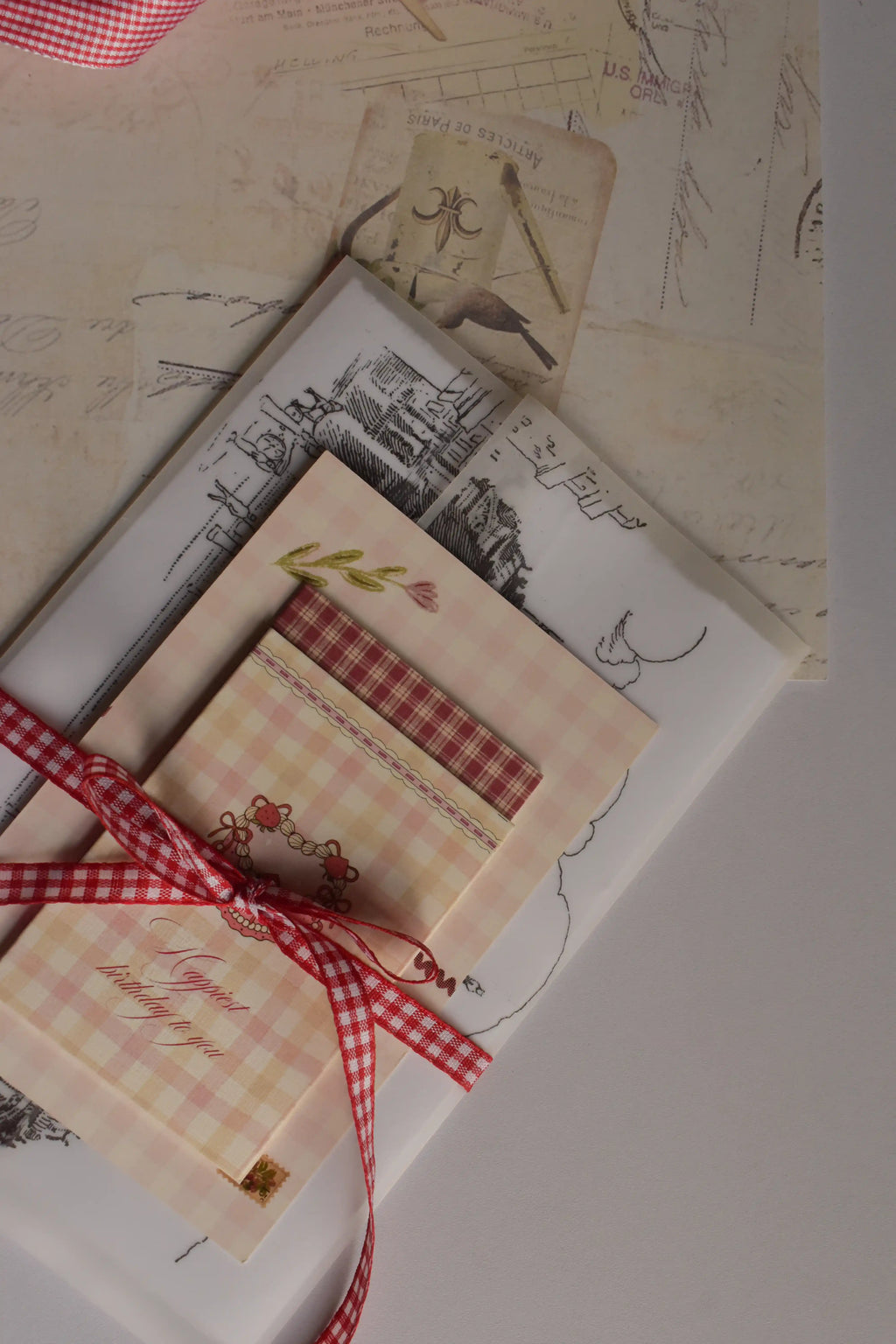 A styled flat lay of the Timeless Love Birthday Bundle featuring the Classic Scarlet Letter, I Just Called To Say I Love You Postcard, Mi Amor Por Ti Greeting Card and Happiest Birthday To You Mini Greeting Card, beautifully wrapped with a red gingham ribbon.