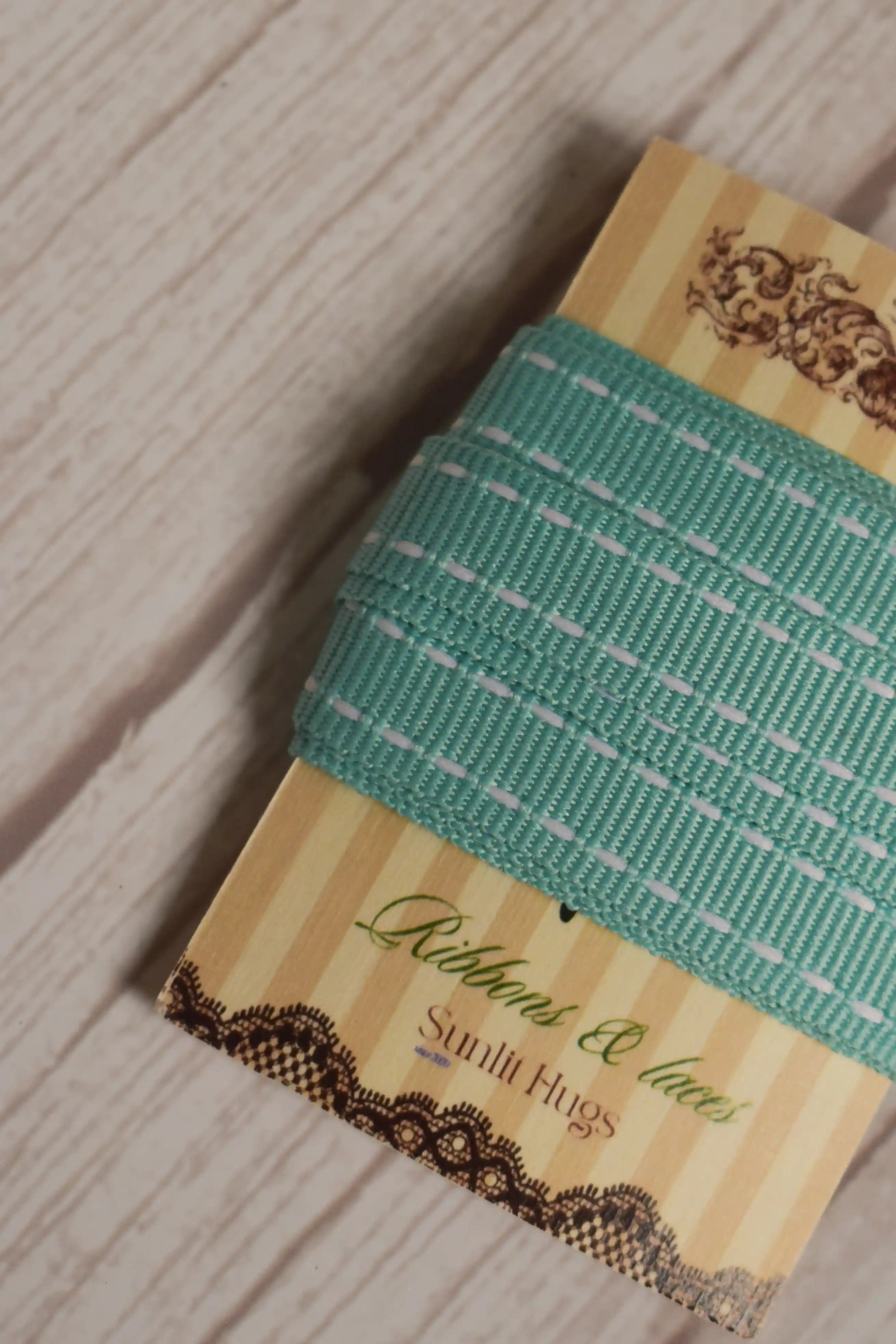 A close-up of Turquoise stitches Ribbon wrapped around a striped Sunlit Hugs ribbon card, showing its turquoise colour and white stitched detailing.