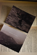 Flat lay of the Vintage Mountain Poetry Photo Print Set resting on the pages of a classic novel, showcasing two 3x4 inch monochrome fine art prints—a Pahari elder portrait and a sweeping mountain landscape—featuring nostalgic Hindi poetry overlays.