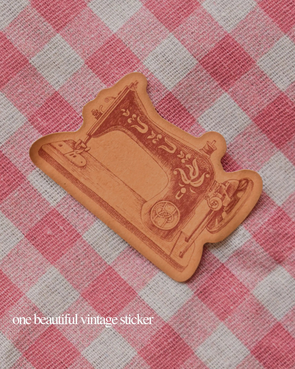 Single vintage die-cut sticker shaped like an antique sewing machine, set against a pink and white checkered background.