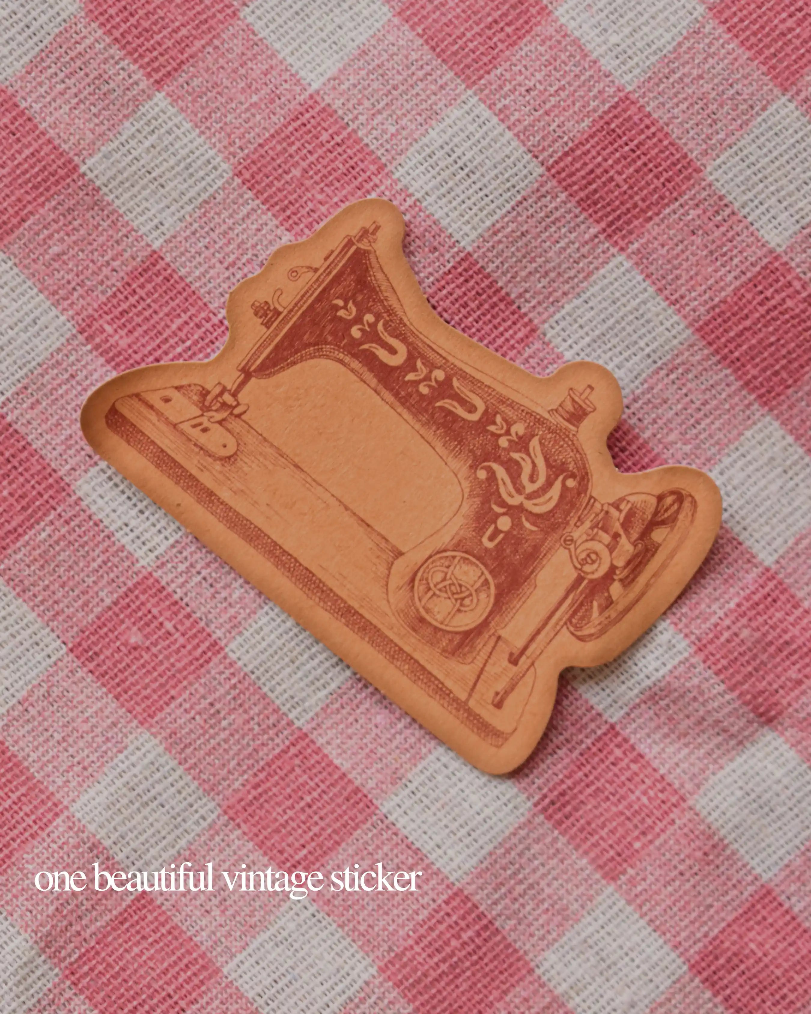 Single vintage die-cut sticker shaped like an antique sewing machine, set against a pink and white checkered background.
