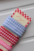 Angled close-up of the wide light blue and wide red gingham ribbons, emphasizing the texture and checkered pattern over the 'Picnic Laces' card.